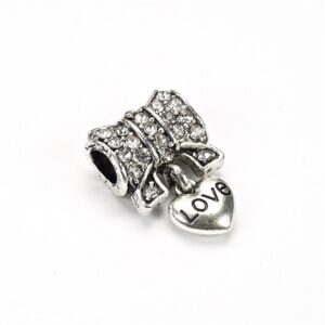 Une perle en maillechort avec un pendentif nœud orné de strass blancs et d'un cœur.